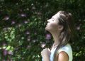Woman Closing Her Eyes Against Sun Light Standing Near Purple Petaled Flower Plant