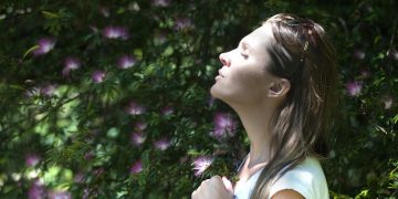 Woman Closing Her Eyes Against Sun Light Standing Near Purple Petaled Flower Plant