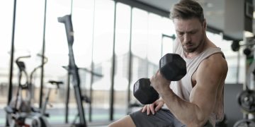 Man in White Tank Top and Grey Shorts Lifting Dumbbell