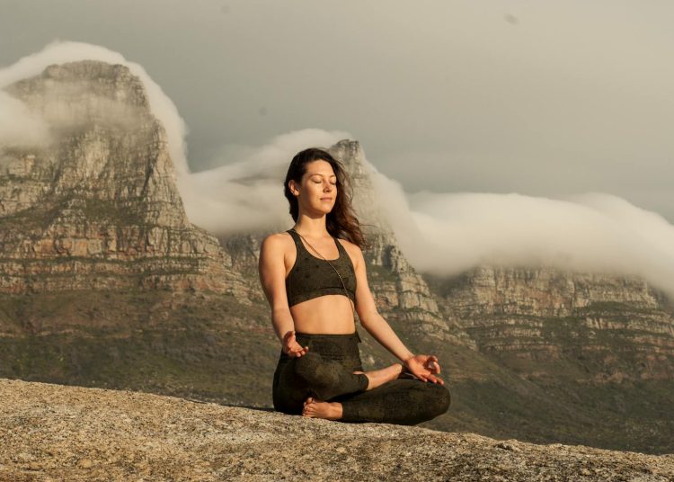 Woman in Black Sports Bra and Black Pants Sitting on Rock