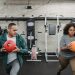 Young muscular ethnic male instructor in activewear doing lunges exercise with ball near plus size black woman during training in sport club