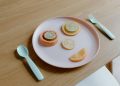 From above of plastic plate with sliced grapefruit orange lemon and lime making face near spoon and fork