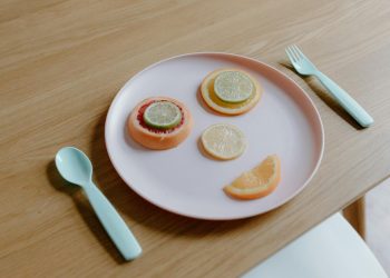 From above of plastic plate with sliced grapefruit orange lemon and lime making face near spoon and fork