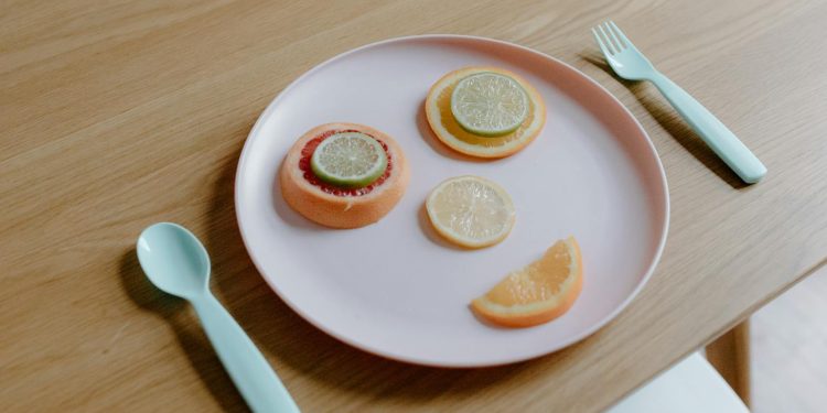 From above of plastic plate with sliced grapefruit orange lemon and lime making face near spoon and fork